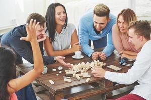 groupe d'amis créatifs assis à une table en bois. les gens s'amusent en jouant à un jeu de société photo