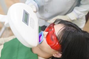 une femme portant des lunettes de protection examinant par stomatologue , blanchiment des dents par lampe ultraviolette photo