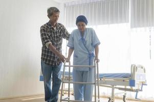 homme âgé aidant une femme patiente atteinte d'un cancer portant un foulard avec une marchette à l'hôpital, des soins de santé et un concept médical photo