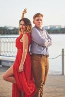 heureuse belle femme en robe rouge et jeune homme danse de l'été avec lac en arrière-plan. contraste des couleurs rouge et blanc photo