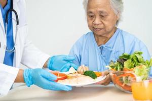 patiente asiatique âgée ou âgée, femme âgée, mangeant le petit-déjeuner et des aliments sains à base de légumes avec espoir et heureuse assise et affamée sur le lit à l'hôpital. photo