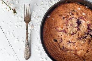 tarte aux cerises sur un fond en bois blanc. à proximité se trouve une vieille cuillère en argent et une floraison printanière. photo