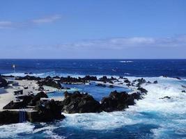 piscines naturelles au milieu de l'océan atlantique à porto moniz, île de madère, portugal. des moments de vacances incroyables. nuages avec soleil. l'océan et les vagues frappant les rochers. les gens dans l'eau. photo