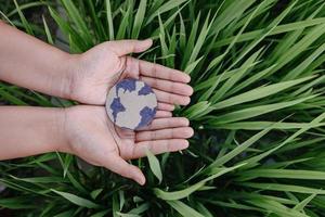 sauver la terre pour le concept de modes de vie durables, protéger la planète terre pour des ressources durables. mains humaines tenant le symbole du globe sur fond de feuilles d'herbe. jour de la terre et développement durable. photo