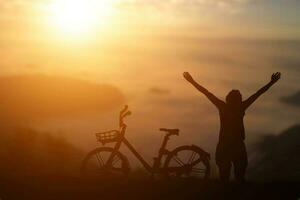 silhouette d'homme leva la main avec un vélo sur fond de coucher de soleil. photo