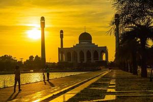 mosquée centrale de songkhla de jour comme de nuit avec un ciel coloré au coucher du soleil et les lumières de la mosquée et des reflets dans l'eau dans un concept de paysage emblématique photo