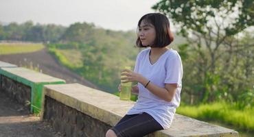 jeune femme asiatique a bu et fait une pause après avoir fait du jogging le matin photo