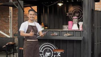 Asian man in bar tablier portant une liste de menus signe ok dans un conteneur thème angkringan photo