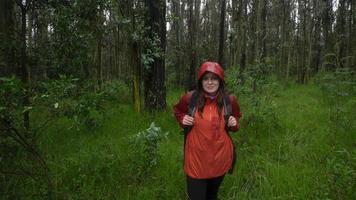 femme hispanique avec sac à dos noir et veste imperméable rouge marchant sur un sentier boueux à travers une forêt pendant la journée photo