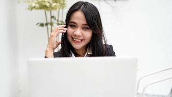 jeune femme d'affaires asiatique travaillant sur ordinateur et parlant sur smartphone au bureau photo