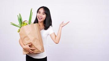 belle femme asiatique tenant un sac en papier de légumes frais très heureux pointant avec la main et le doigt sur fond blanc isolé photo
