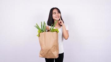 femme asiatique pensant avec sac en papier de légumes frais avec fond blanc isolé photo