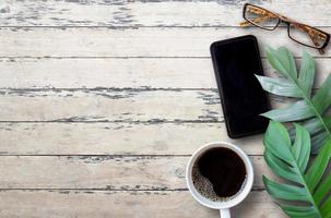 vue de dessus avec smartphone, verres, tasse de café et congé vert sur fond de table en bois. photo