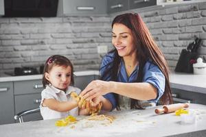 famille heureuse dans la cuisine. concept de nourriture de vacances. mère et fille préparent la pâte, préparent des biscuits. famille heureuse en faisant des biscuits à la maison. nourriture maison et petit assistant photo