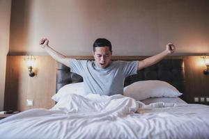 portrait d'un homme bâillant tout en étirant ses bras dans son lit photo