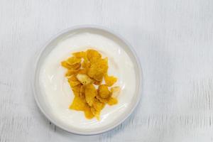 le yaourt dans une tasse en céramique a des flocons de maïs sur fond de bois blanc. photo