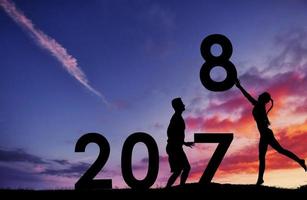 silhouette de l'homme et de la fille qui détient les chiffres de la nouvelle année au coucher du soleil. concept de remplacement 2017 à 2018 photo