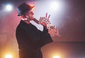 magicien montrant un tour avec des cartes à jouer. magie ou dextérité, cirque, jeux d'argent. prestidigitateur dans une pièce sombre avec brouillard photo