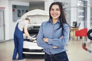 femme dans un garage automobile obtenant un service mécanique. le mécanicien travaille sous le capot de la voiture photo