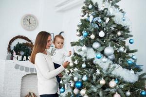 mère de famille heureuse et bébé décorent l'arbre de noël photo