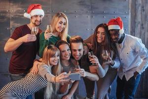 grouper de beaux jeunes faisant du selfie à la fête du nouvel an, les meilleurs amis filles et garçons s'amusant ensemble, posant des personnes au style de vie émotionnel. chapeaux pères noël et verres de champagne dans leurs mains photo