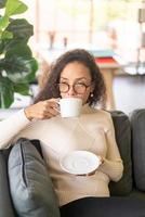 femme latine buvant du café sur un canapé à la maison photo