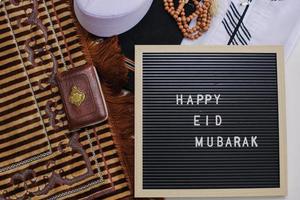 vue de dessus de la robe musulmane et des perles de prière avec le livre saint d'al quran et le tableau des lettres dit joyeux eid mubarak. il y a une lettre arabe qui signifie le livre saint photo