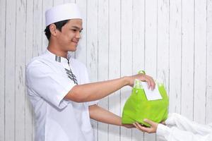 homme musulman religieux donnant l'aumône sous forme de nourriture dans un sac vert et une enveloppe blanche remplie d'argent photo