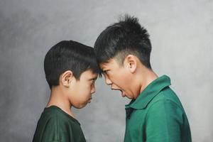 deux frères et sœurs se regardant et grand frère criant devant son petit frère sur fond gris photo