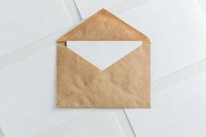 carte blanche vierge dans une enveloppe kraft marron et modèle de feuilles de papier maquette photo