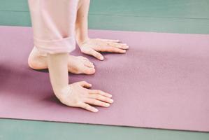 mains et jambes d'une femme faisant du yoga sur un tapis de yoga. rituels de soins personnels, méditation et santé mentale, calme et relaxation. vue de côté photo