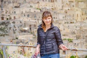 belle jeune femme voyageuse avec une veste noire regardant la caméra, souriant, posant et gardant l'épillet dans les sassi di matera photo