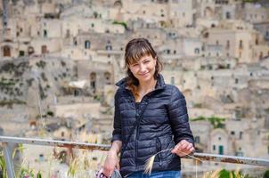 belle jeune femme voyageuse avec une veste noire regardant la caméra, souriant, posant et gardant l'épillet dans les sassi di matera photo