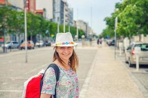 jeune femme voyageur avec chapeau regardant la caméra posant et souriant dans les rues de la ville d'aveiro au portugal photo