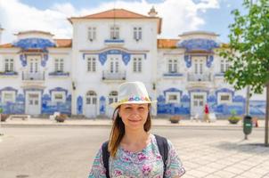 jeune femme voyageur avec chapeau regardant la caméra posant et souriant dans les rues de la ville d'aveiro au portugal photo