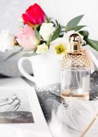 bouteille de parfum. bouquet de printemps sur table en béton gris. roses, tulipes et lisianthus. plume blanche. photo