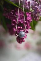 collier en pierre naturelle avec garnitures en argent avec des fleurs de lilas violet violet sur une plume d'autruche blanche. accessoires en argent. photo