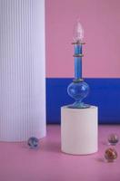 bouteille bleue avec parfum sur un podium blanc sur fond rose et colonnes. présentation cosmétique. maquette de bouteille en verre bleu avec parfum ou huile pour bannière publicitaire photo