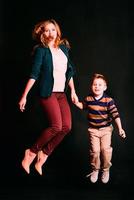 portrait d'un mignon petit garçon élégant avec une belle maman sautant ensemble sur fond sombre en studio photo