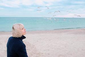 femme blonde et mouettes par temps nuageux sur la côte de la mer photo