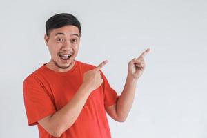 expression du visage souriant et surpris d'un homme asiatique heureux en t-shirt rouge avec la main pointant sur l'espace vide photo