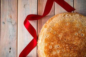 gros plan de crêpes minces russes traditionnelles sur un fond en bois clair et un ruban rouge. photo