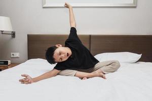 garçon asiatique paresseux qui s'étire et bâille sur le lit photo
