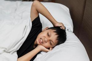 garçon asiatique souffrant de maux de dents et ressentant de la douleur en étant allongé sur le lit photo