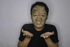 sourire homme asiatique pointant dans la main quand il utilise un masque de beauté photo