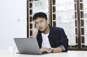 jeune homme asiatique se sentant stressé et confus lorsqu'il travaille un ordinateur portable sur la table. photo