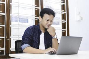 jeune homme asiatique se sentant sérieux lorsqu'il travaille un ordinateur portable sur la table. photo