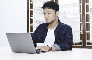 jeune homme asiatique se sentant sérieux lorsqu'il travaille un ordinateur portable sur la table. photo