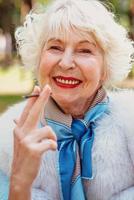 femme senior élégante et élégante souriante à la mode avec des cheveux gris en manteau de fourrure cigarette en plein air. mode de vie malsain, âge, vibrations positives, vieillesse, dépendance, concept de mauvaise habitude. photo