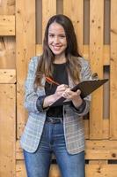 femme souriante avec stylo et tablette près d'un mur en bois photo